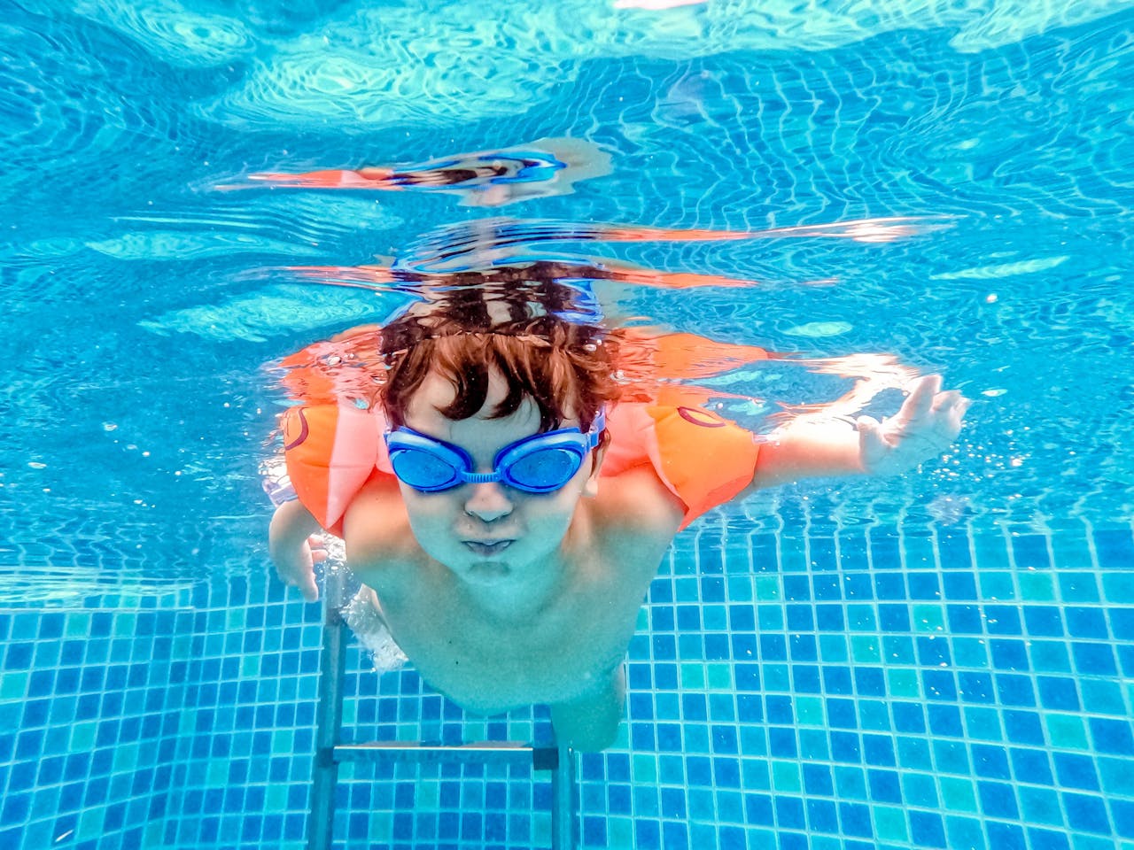 A young child swimming with water wings and goggles in a home swimming pool